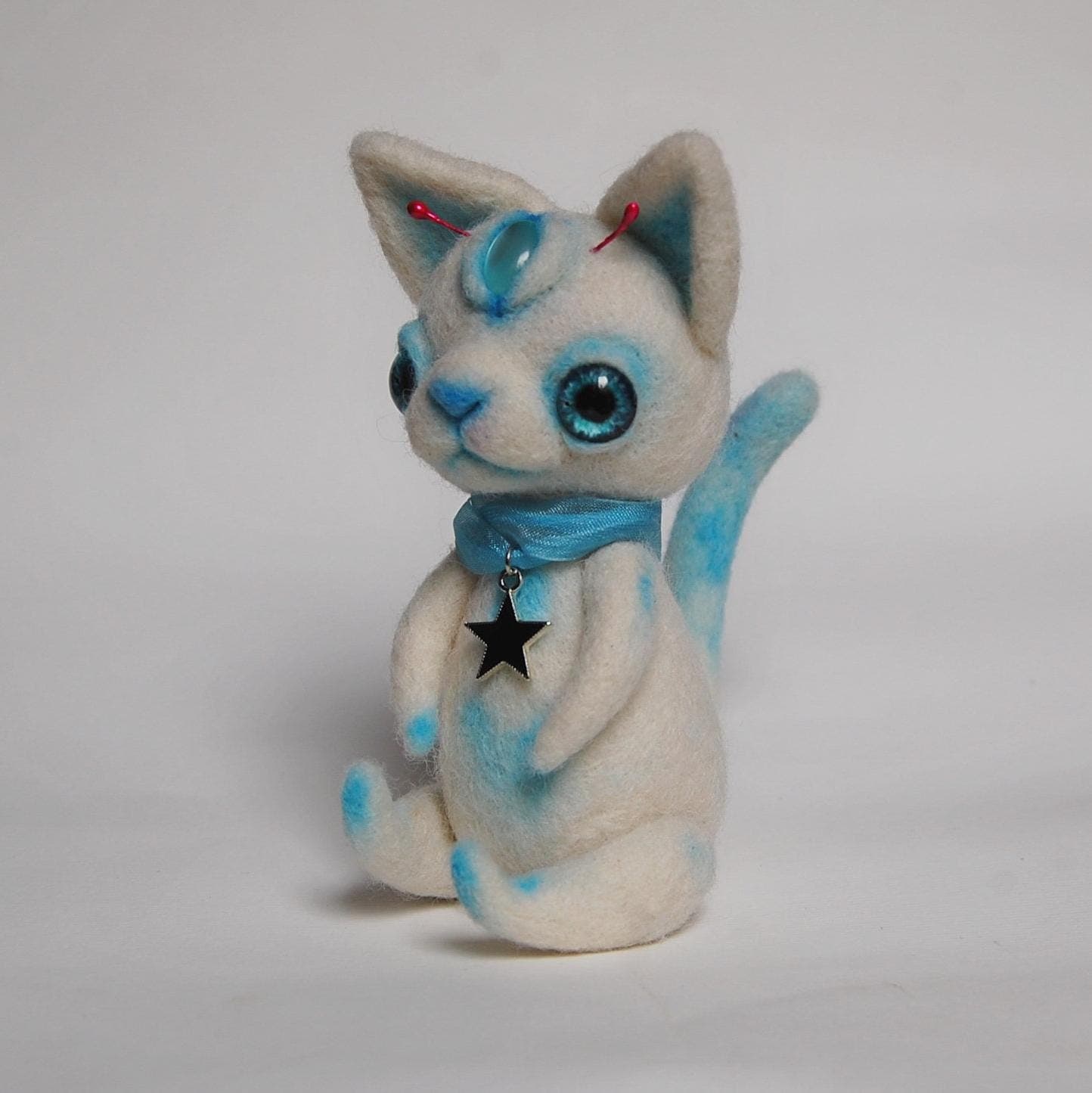 Needle-felted white cat figure with blue accents, large eyes and a star pendant